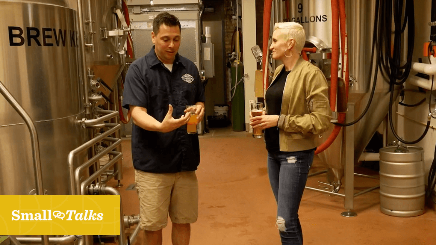 Man holding beer talking to woman holding beer in brewery